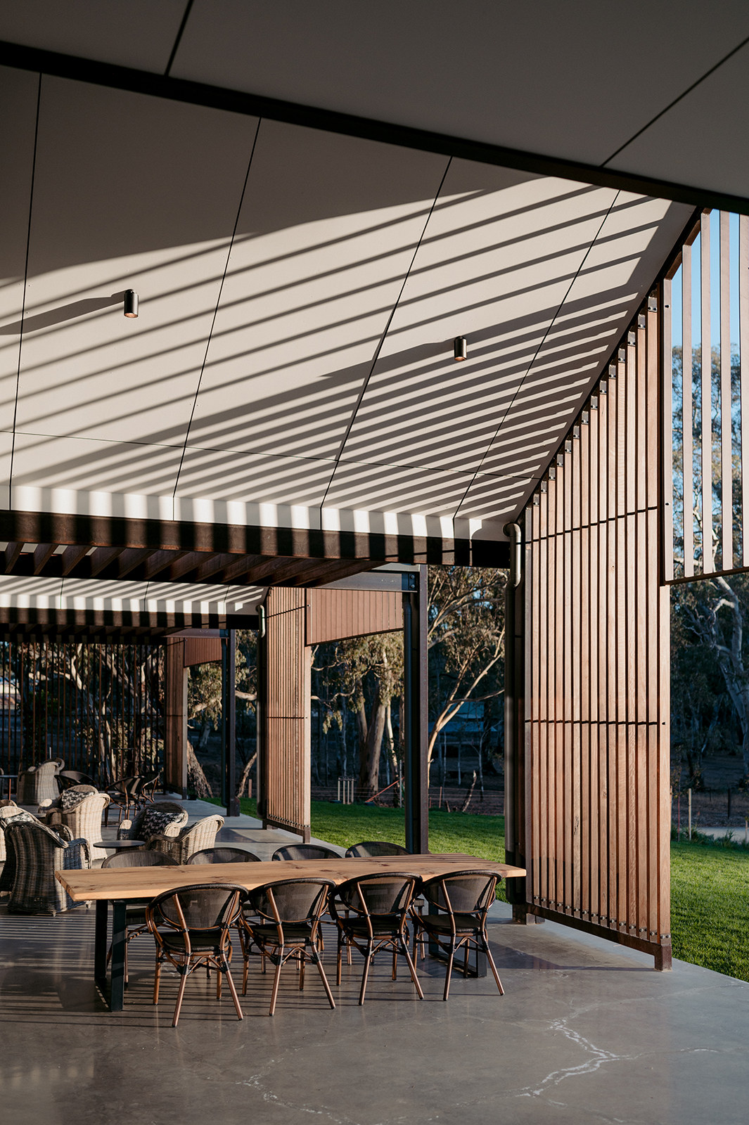 Covered terrace with festoon lights between timber-clad pavilions, looking out to the lawn