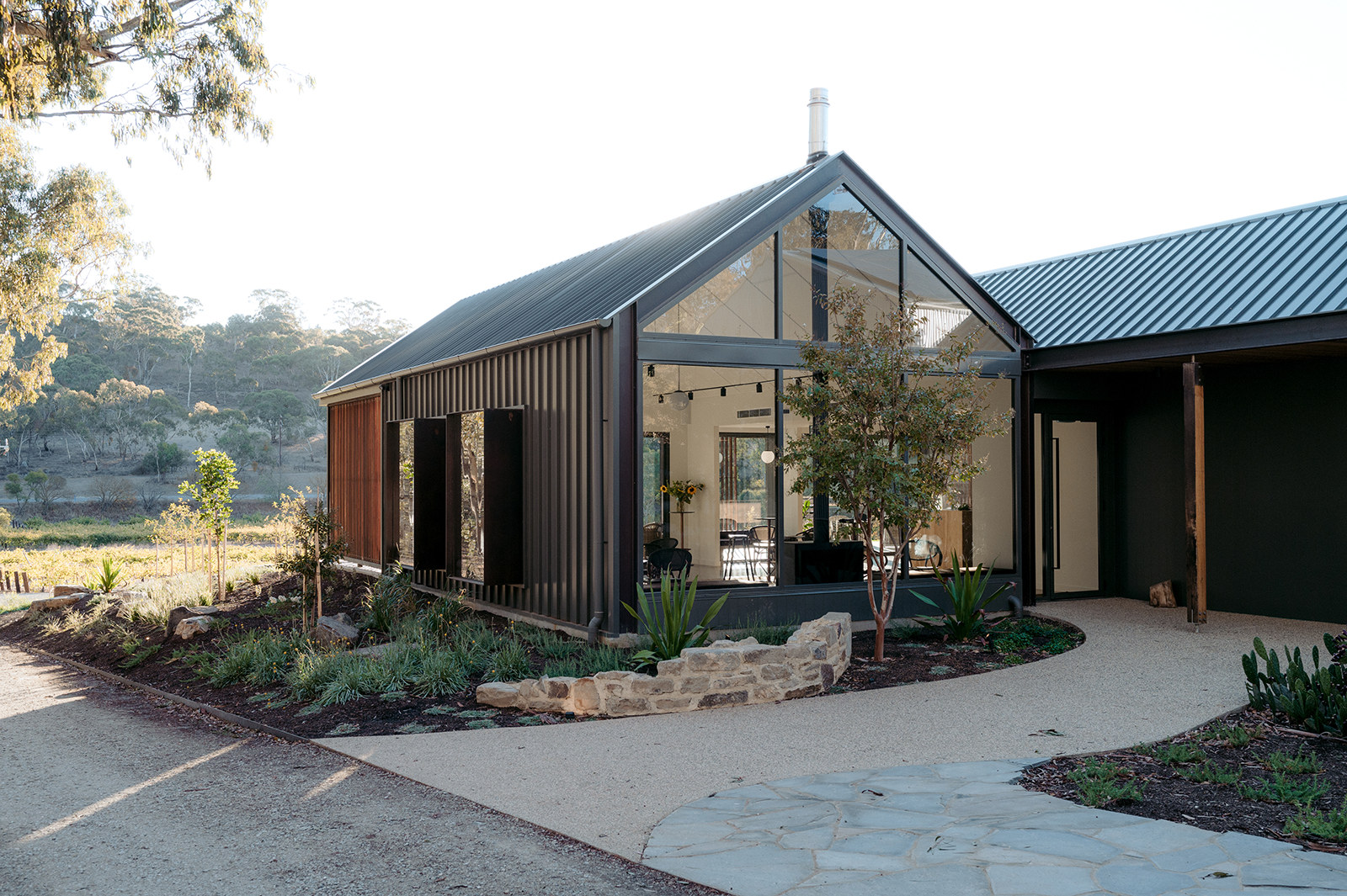 Three gabled pavilions in a row at dusk, lights on, lawn in front