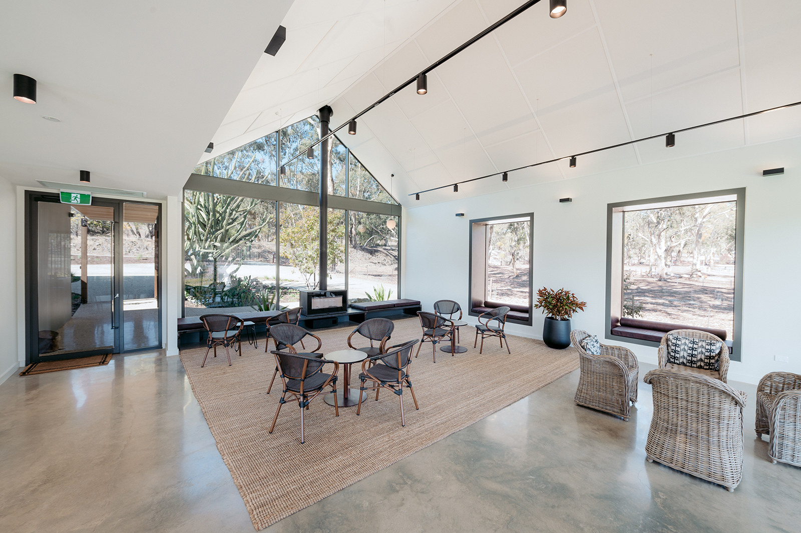 Light-filled gabled interior with a glazed end wall, cafe chairs on a jute rug and polished concrete floor