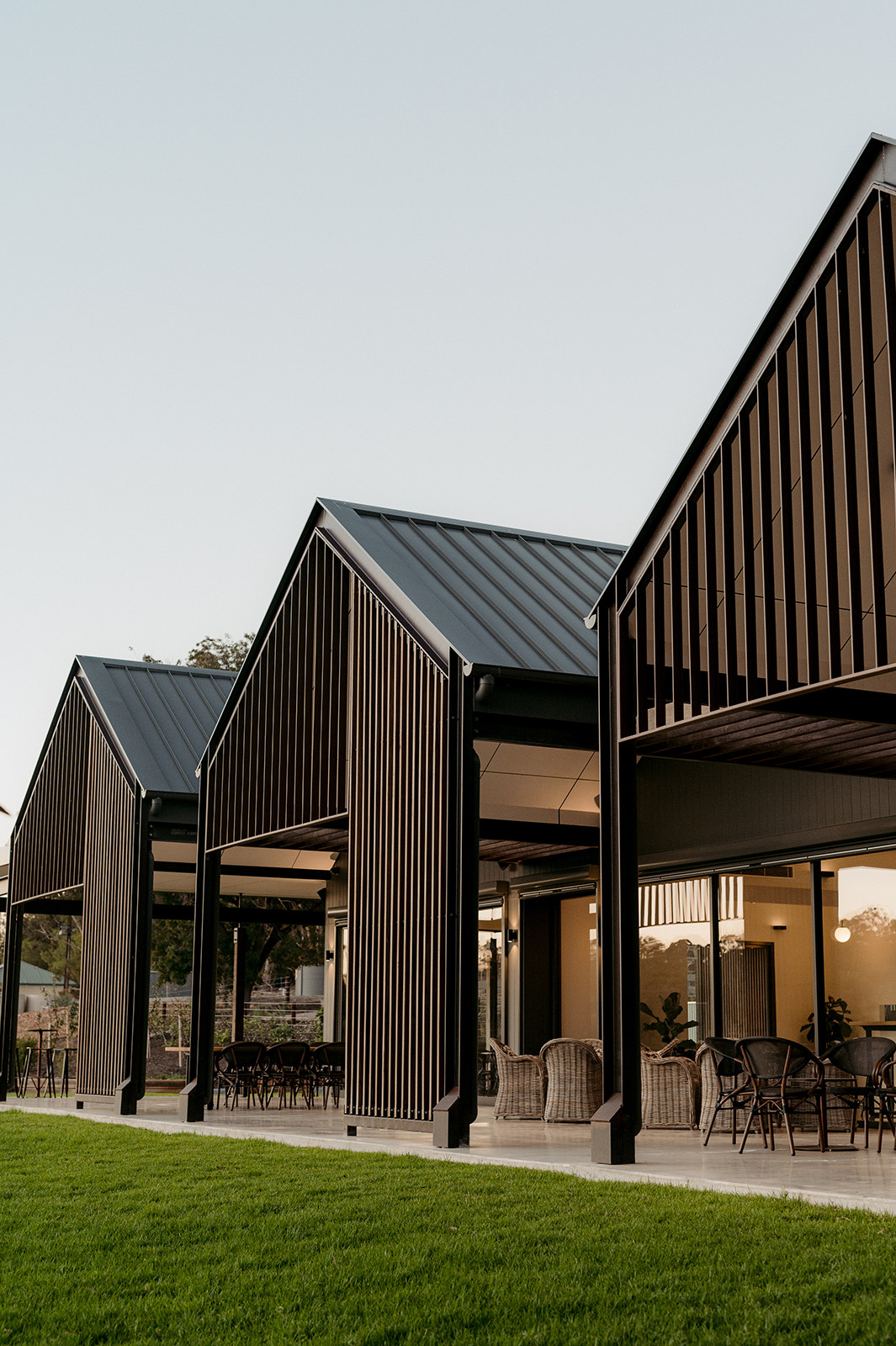 Row of black-battened gable pavilions opening onto a lawn