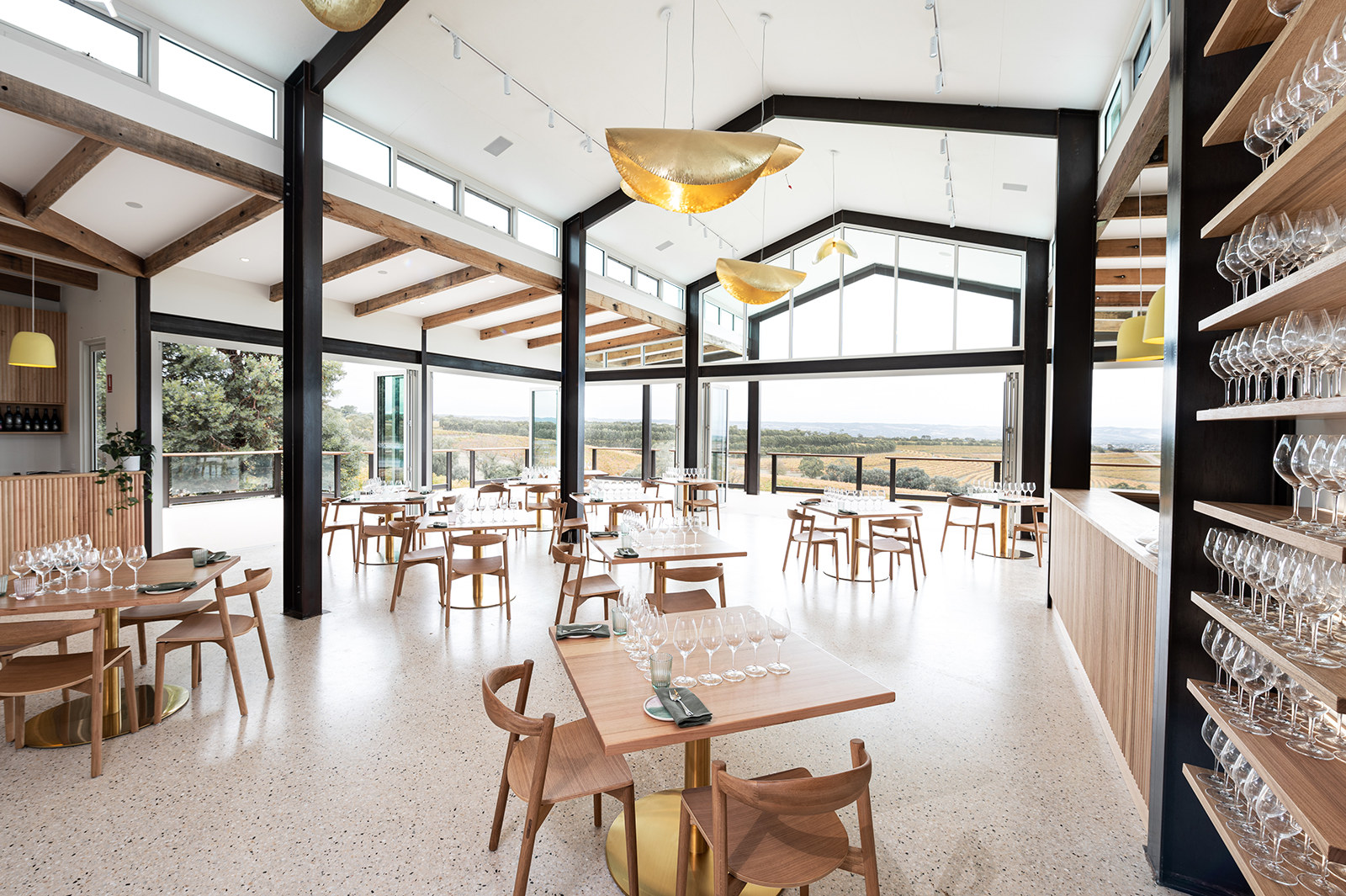 Sunlit timber-lined dining room with pendant lights, cafe tables and full-height glazing to the garden