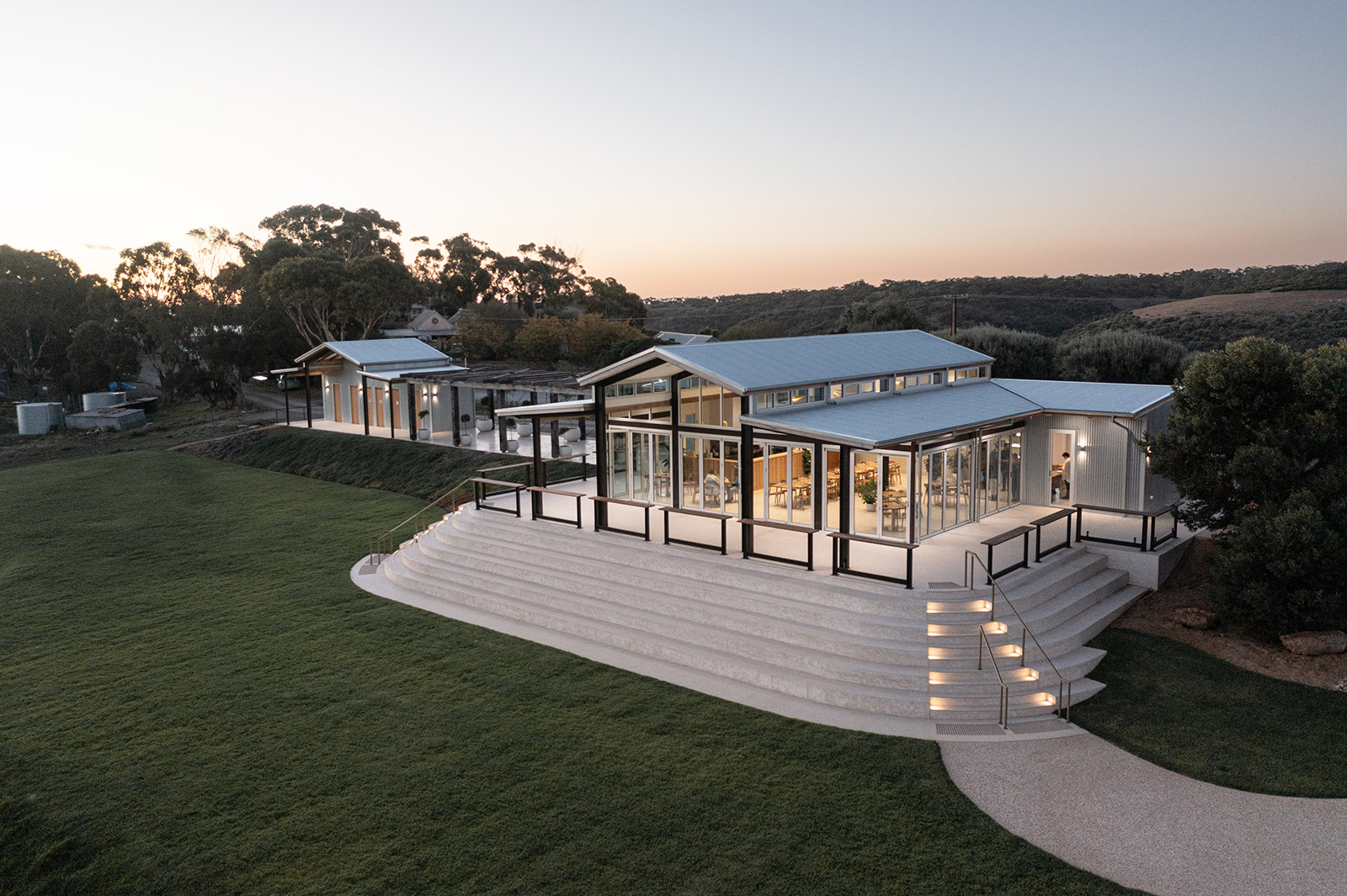 Hills Cellar Door at dusk, wide lawn and stepped terrace leading to the pavilion
